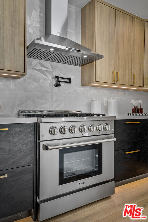 kitchen with light hardwood / wood-style flooring, wall chimney exhaust hood, backsplash, and high end stainless steel range