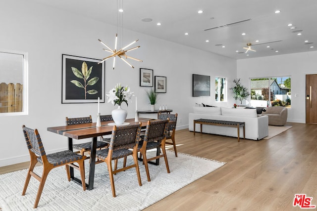 dining room with a high ceiling, ceiling fan with notable chandelier, and light hardwood / wood-style flooring