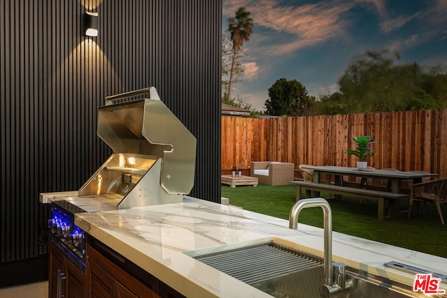 patio terrace at dusk with a lawn, an outdoor kitchen, and sink