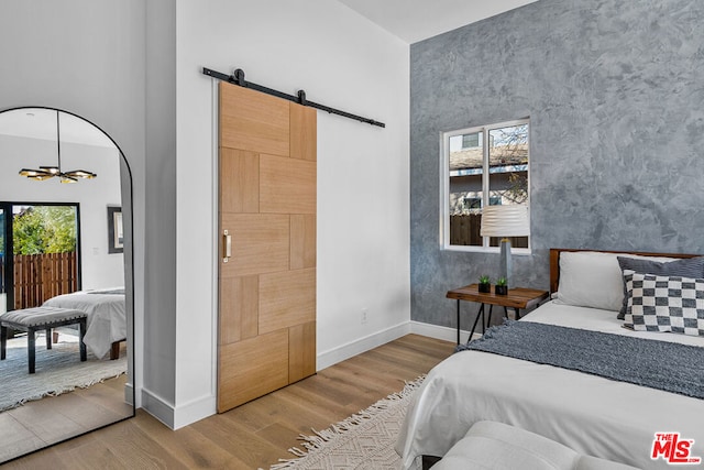 bedroom with a high ceiling, a barn door, an inviting chandelier, and hardwood / wood-style flooring