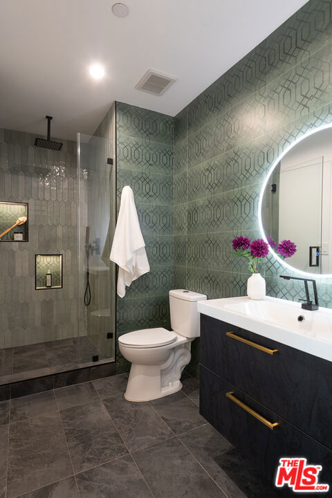 bathroom with toilet, a tile shower, tile walls, and vanity