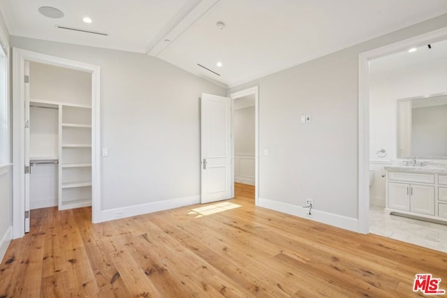 unfurnished bedroom with light wood-type flooring, a walk in closet, and lofted ceiling