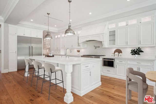 kitchen with sink, white cabinets, tasteful backsplash, and an island with sink