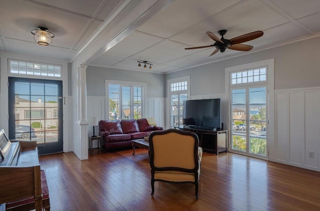 living room with decorative columns, crown molding, dark wood-type flooring, and ceiling fan