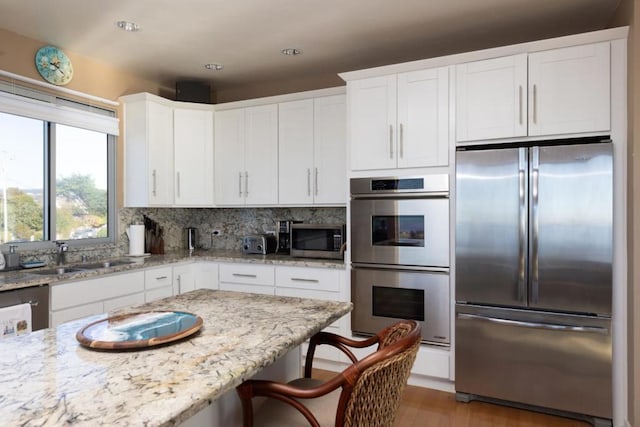 kitchen with light stone counters, sink, white cabinets, and stainless steel appliances