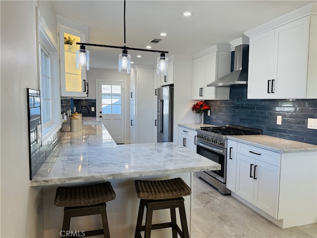 kitchen with a kitchen bar, white cabinetry, wall chimney range hood, stainless steel appliances, and kitchen peninsula