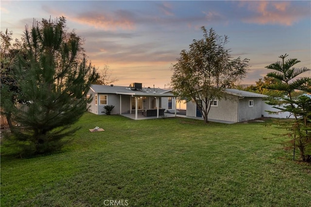 back house at dusk featuring a patio area and a lawn