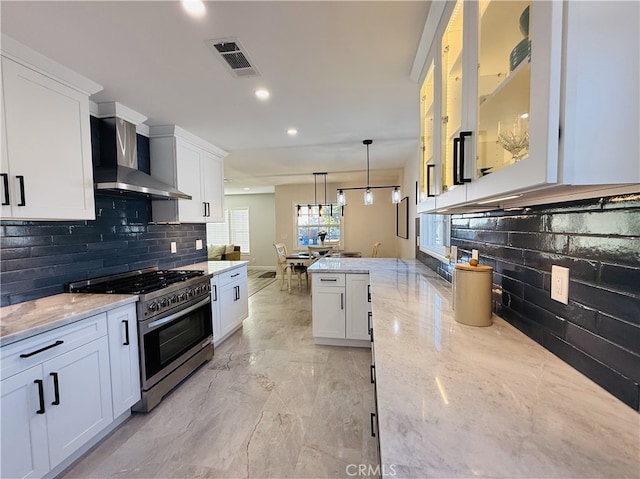 kitchen with pendant lighting, white cabinetry, stainless steel range with gas stovetop, light stone counters, and wall chimney range hood