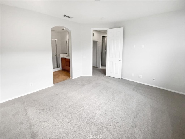 unfurnished bedroom with arched walkways, visible vents, light carpet, ensuite bath, and baseboards