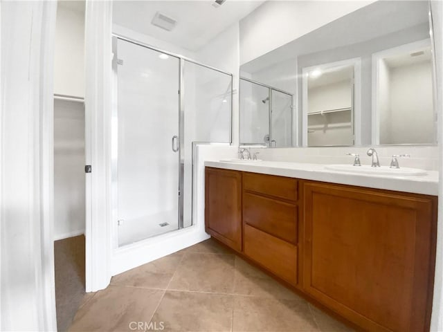 bathroom with double vanity, a spacious closet, a sink, a shower stall, and tile patterned floors