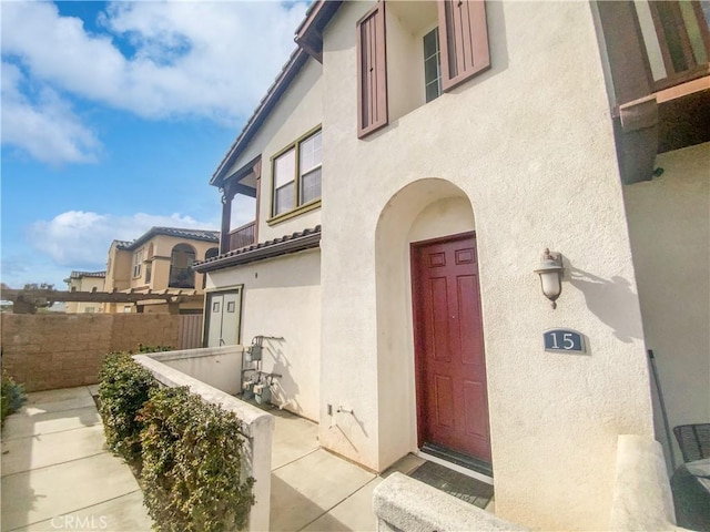 view of exterior entry with fence and stucco siding