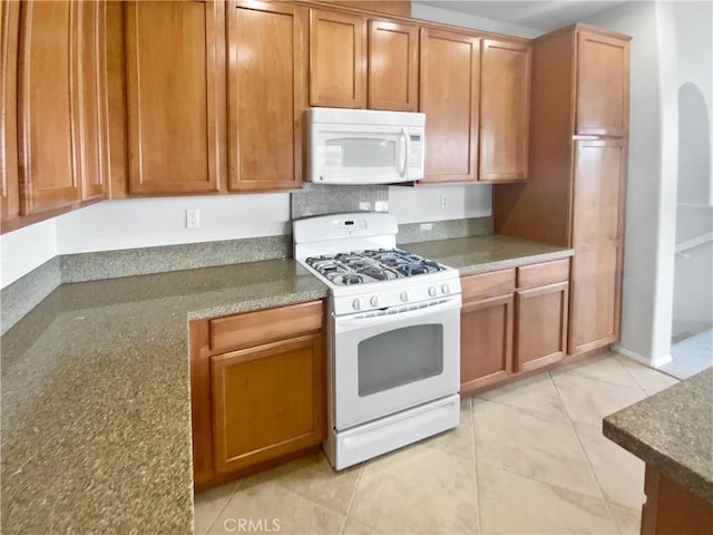 kitchen with white appliances, arched walkways, and brown cabinets