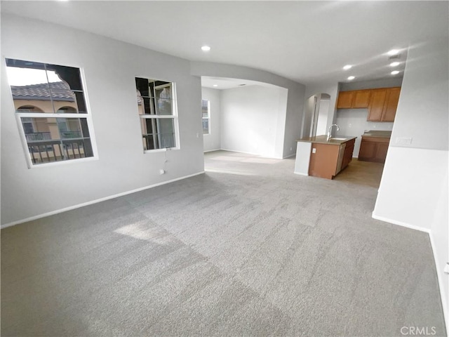 unfurnished living room featuring arched walkways, recessed lighting, light colored carpet, a sink, and baseboards