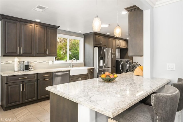 kitchen featuring washer and clothes dryer, appliances with stainless steel finishes, pendant lighting, a breakfast bar, and sink