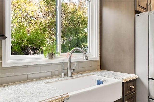 room details with sink, dark brown cabinets, light stone counters, and stainless steel refrigerator