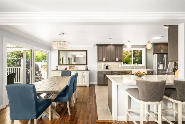 kitchen featuring light stone countertops, crown molding, stainless steel fridge, and decorative light fixtures