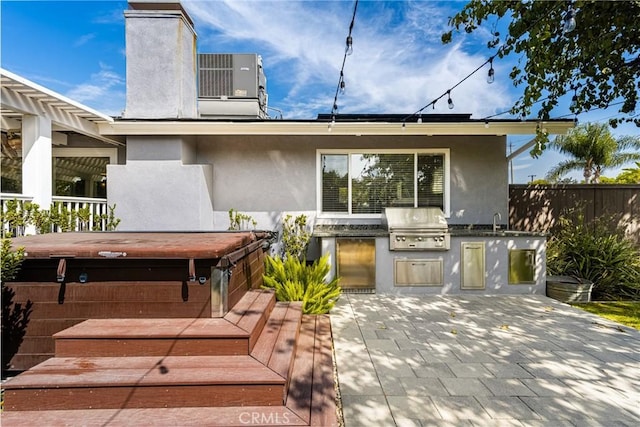 back of house with cooling unit, a hot tub, exterior kitchen, and sink