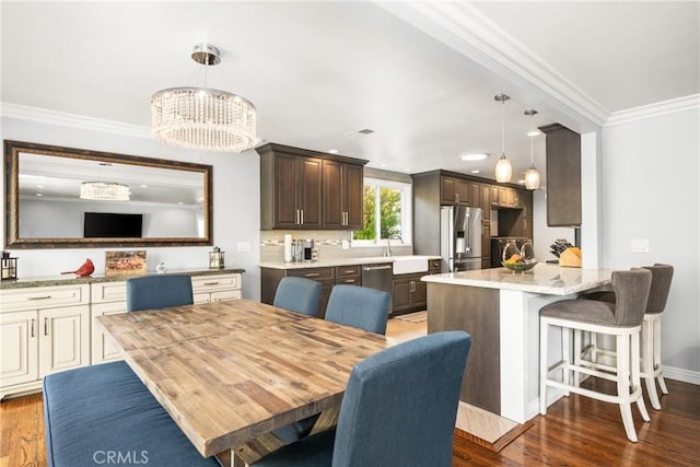 dining area with sink, dark hardwood / wood-style floors, crown molding, and a chandelier