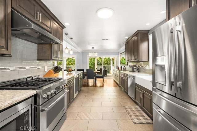 kitchen with decorative backsplash, dark brown cabinetry, hanging light fixtures, stainless steel appliances, and light tile patterned floors