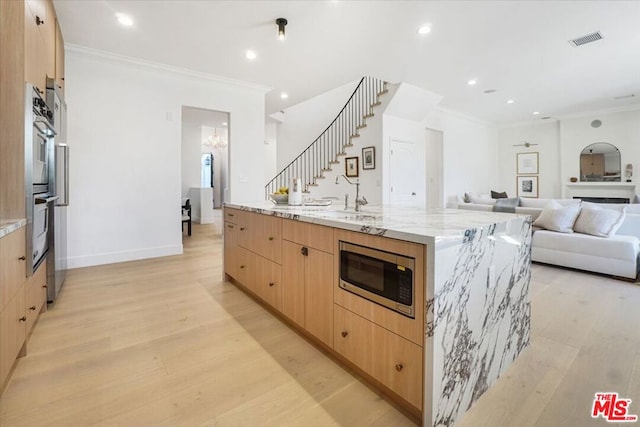 kitchen featuring stainless steel appliances, a spacious island, light wood-type flooring, light stone countertops, and crown molding