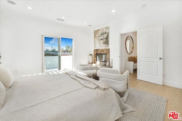 bedroom with light wood-type flooring, access to exterior, crown molding, and a fireplace