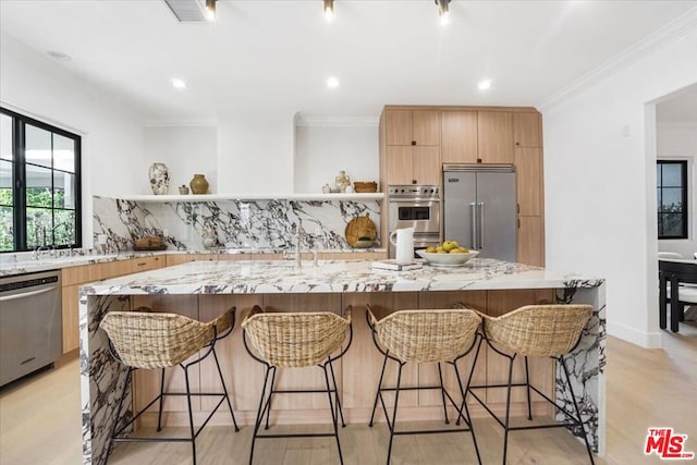 kitchen with stainless steel appliances, a large island with sink, and light stone countertops