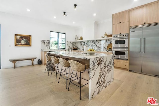 kitchen featuring a kitchen bar, stainless steel appliances, tasteful backsplash, light hardwood / wood-style floors, and a center island with sink