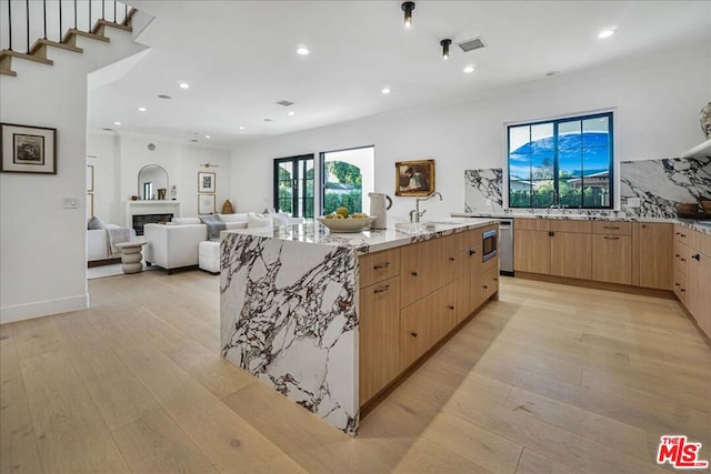 kitchen featuring light brown cabinetry, light stone countertops, a center island with sink, and light hardwood / wood-style floors