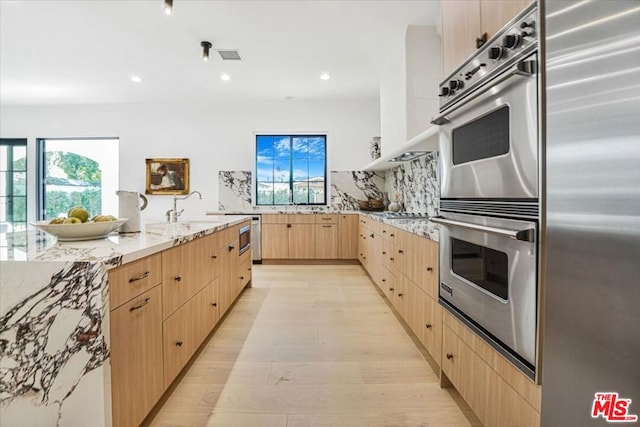 kitchen featuring decorative backsplash, light hardwood / wood-style flooring, appliances with stainless steel finishes, light brown cabinetry, and light stone counters