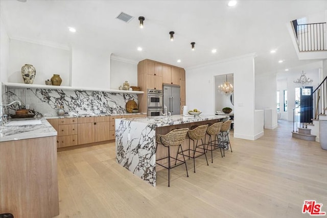 kitchen with a breakfast bar area, backsplash, a large island with sink, light stone counters, and sink