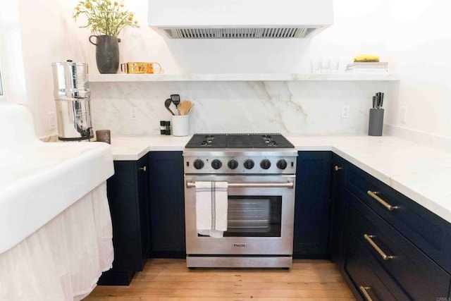 kitchen featuring high end stainless steel range oven, extractor fan, blue cabinetry, backsplash, and light hardwood / wood-style flooring