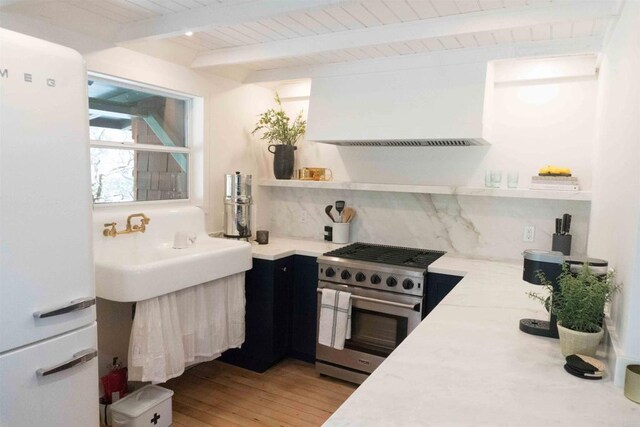 kitchen with beamed ceiling, tasteful backsplash, light hardwood / wood-style floors, stainless steel stove, and wooden ceiling