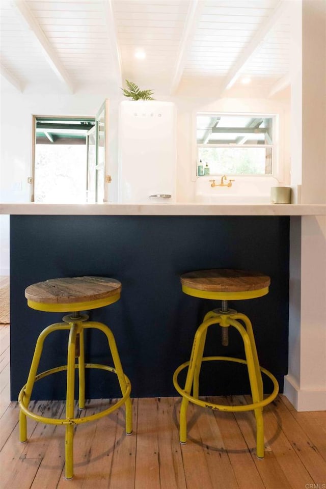 bar featuring light wood-type flooring, a healthy amount of sunlight, and beam ceiling