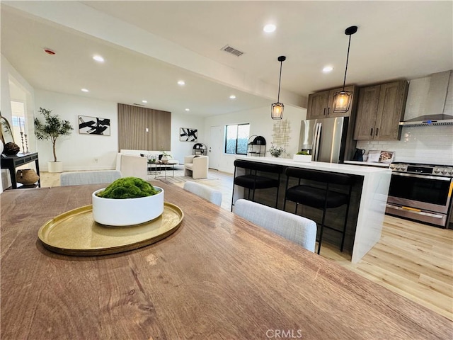 kitchen with appliances with stainless steel finishes, wall chimney range hood, tasteful backsplash, hanging light fixtures, and a breakfast bar area