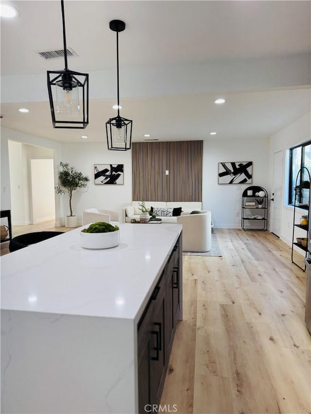 kitchen featuring decorative light fixtures, light wood-type flooring, light stone countertops, a kitchen island, and a chandelier