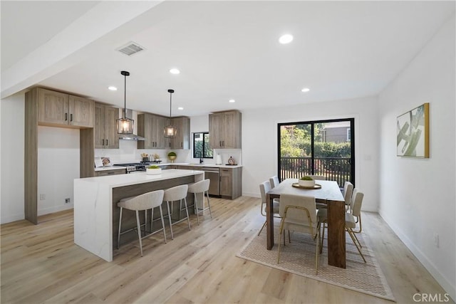 kitchen with appliances with stainless steel finishes, a kitchen island, wall chimney range hood, light hardwood / wood-style floors, and hanging light fixtures