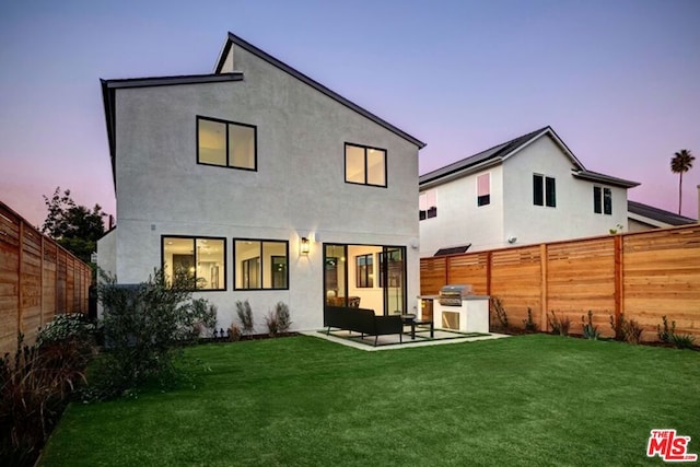 back house at dusk with an outdoor hangout area, an outdoor kitchen, a yard, and a patio