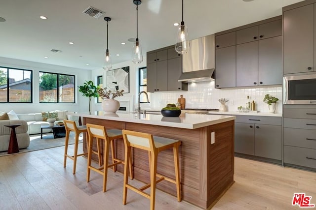 kitchen with sink, wall chimney exhaust hood, an island with sink, and gray cabinetry