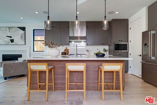 kitchen featuring wall chimney range hood, appliances with stainless steel finishes, a breakfast bar area, and tasteful backsplash