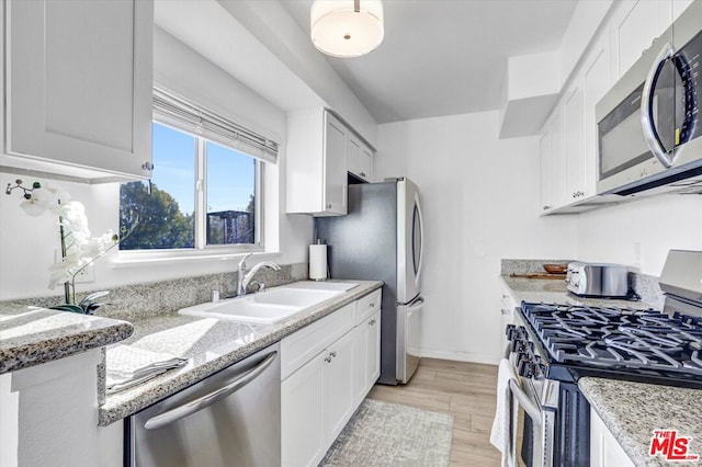 kitchen with light stone countertops, white cabinets, appliances with stainless steel finishes, and sink