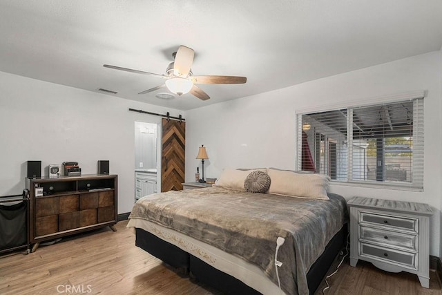 bedroom featuring connected bathroom, ceiling fan, light hardwood / wood-style floors, and a barn door