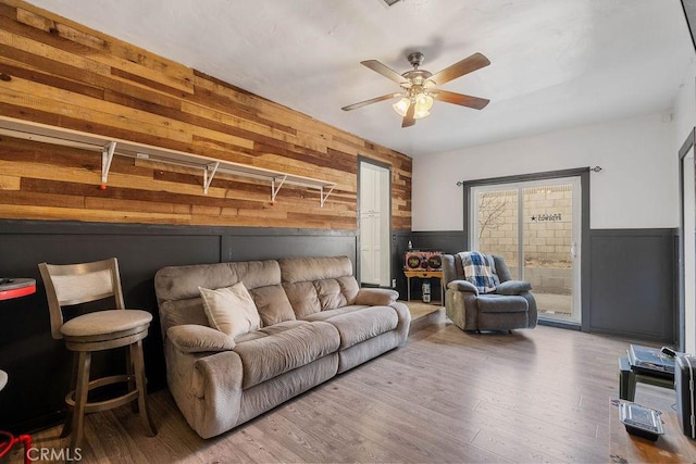 living room featuring ceiling fan, hardwood / wood-style flooring, and wooden walls