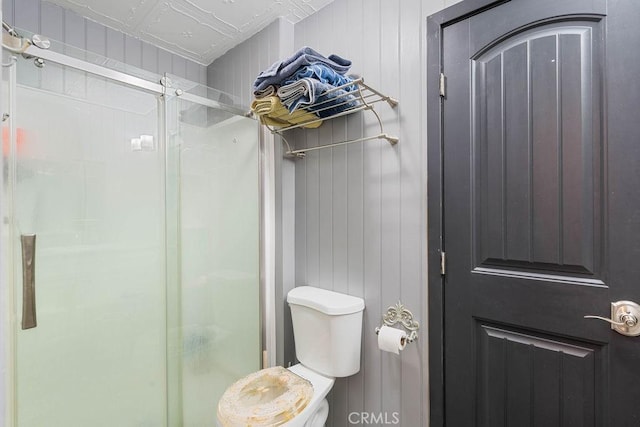 bathroom with toilet, wood walls, and a shower with door