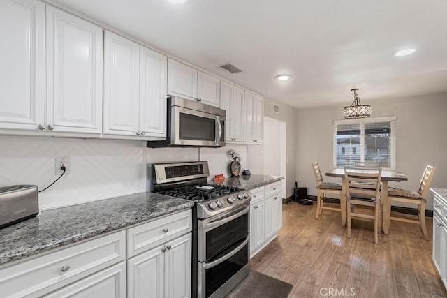 kitchen featuring decorative backsplash, white cabinets, pendant lighting, and appliances with stainless steel finishes