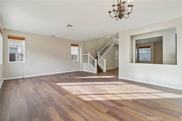 unfurnished living room featuring plenty of natural light, hardwood / wood-style floors, and an inviting chandelier