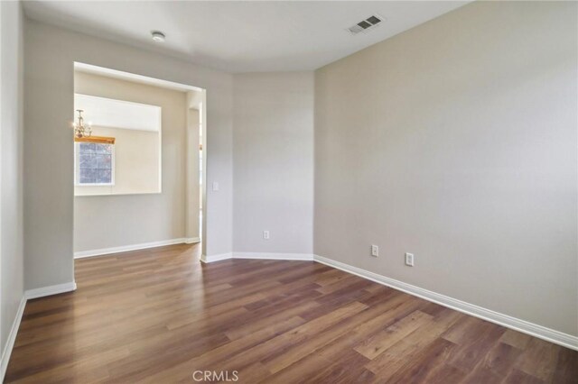 spare room with dark wood-type flooring and an inviting chandelier