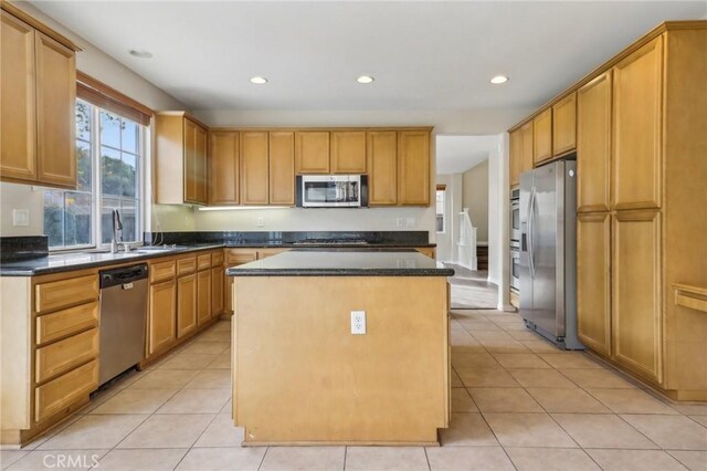 kitchen with sink, appliances with stainless steel finishes, light tile patterned flooring, and a center island