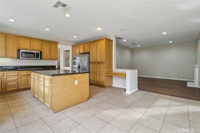 kitchen with dark stone countertops, light tile patterned flooring, appliances with stainless steel finishes, and a kitchen island