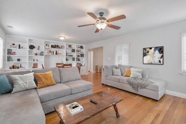 living room featuring built in features, ceiling fan, light hardwood / wood-style floors, and a wealth of natural light