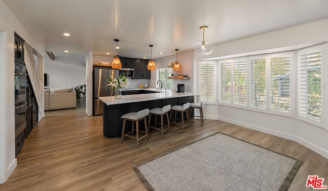 kitchen with appliances with stainless steel finishes, hanging light fixtures, kitchen peninsula, hardwood / wood-style flooring, and a breakfast bar area